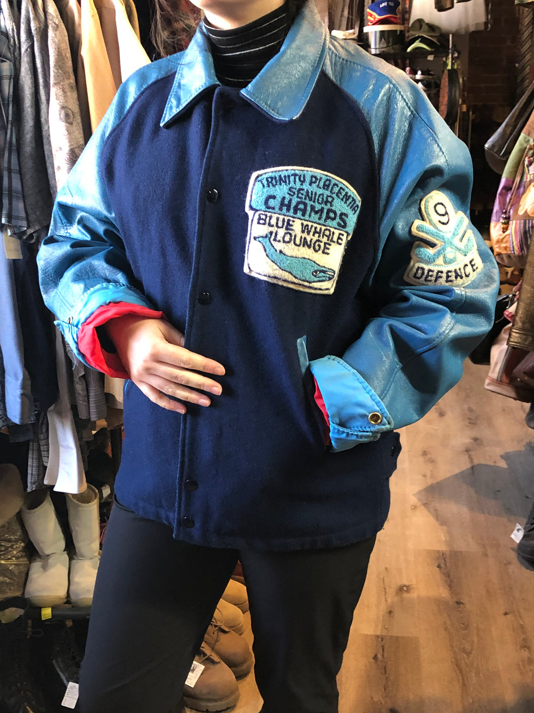 Trinity Placentia Senior Champs “Blue Whale Lounge “ blue varsity jacket with snap closures, slash pockets, embroidered emblem on chest and arm, “whalers” written across the back and a red lining. Size 44.